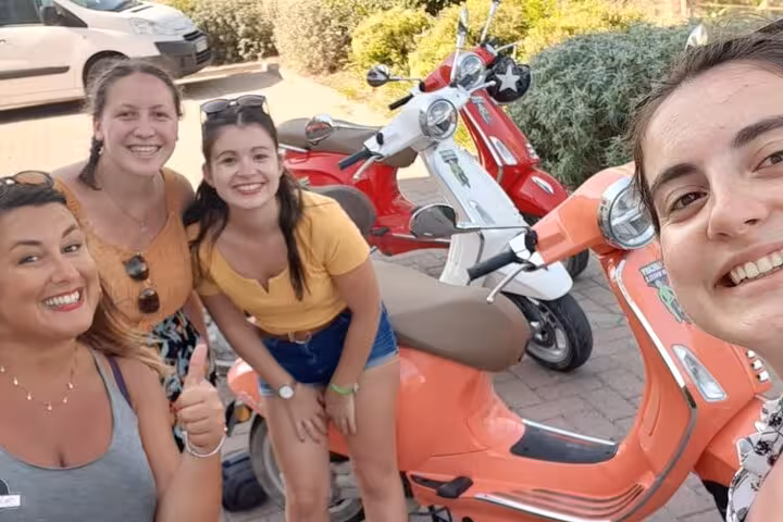 Group of friends smiling next to colorful Vespas, ready for a Tuscany tour from Florence with lunch and wine.