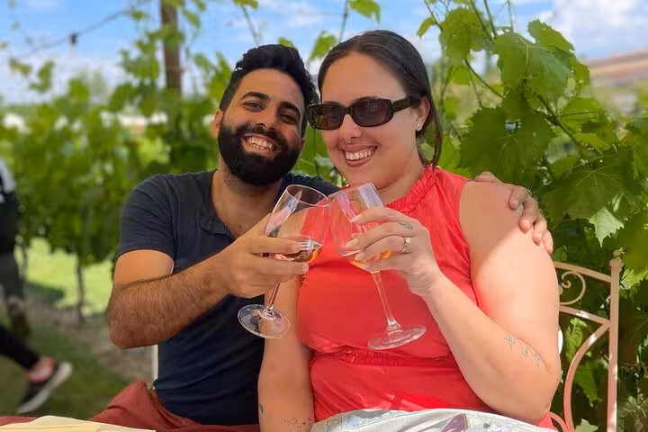 Couple toasting with wine glasses under a lush vineyard canopy in Tuscany.