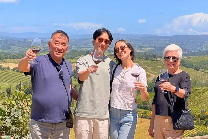 Group enjoying wine tasting with a scenic view of Tuscany's vineyards on a sunny day during their tour.