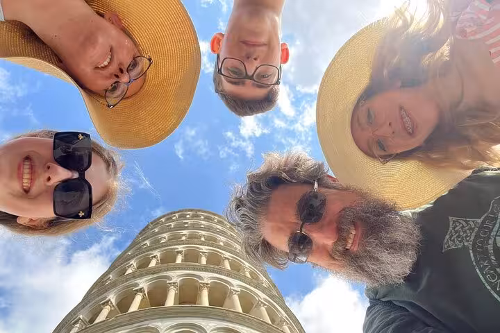 Group of tourists joyfully pose around the Leaning Tower of Pisa, capturing a fun moment on their Tuscany trip.