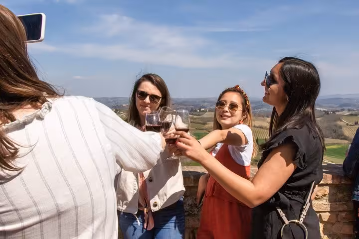 Friends toasting with wine glasses against the backdrop of Tuscany's rolling hills in a small group tour setting.