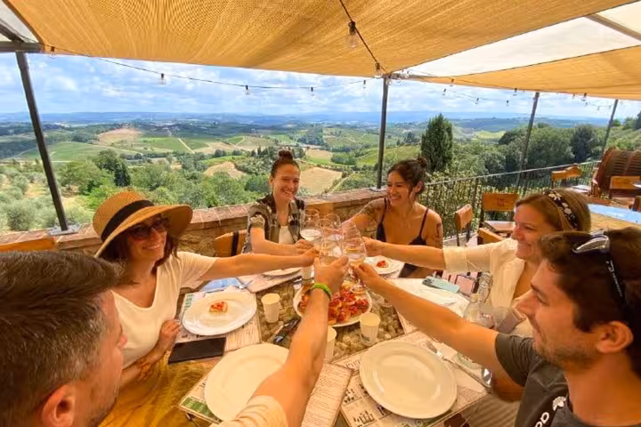 Travelers toasting with wine at an outdoor restaurant overlooking Tuscany's rolling hills.