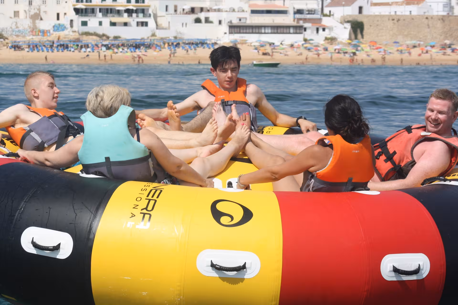Group of tourists enjoying a fun Twister inflatable tube water sport adventure near a sunny Algarve beach coastline
