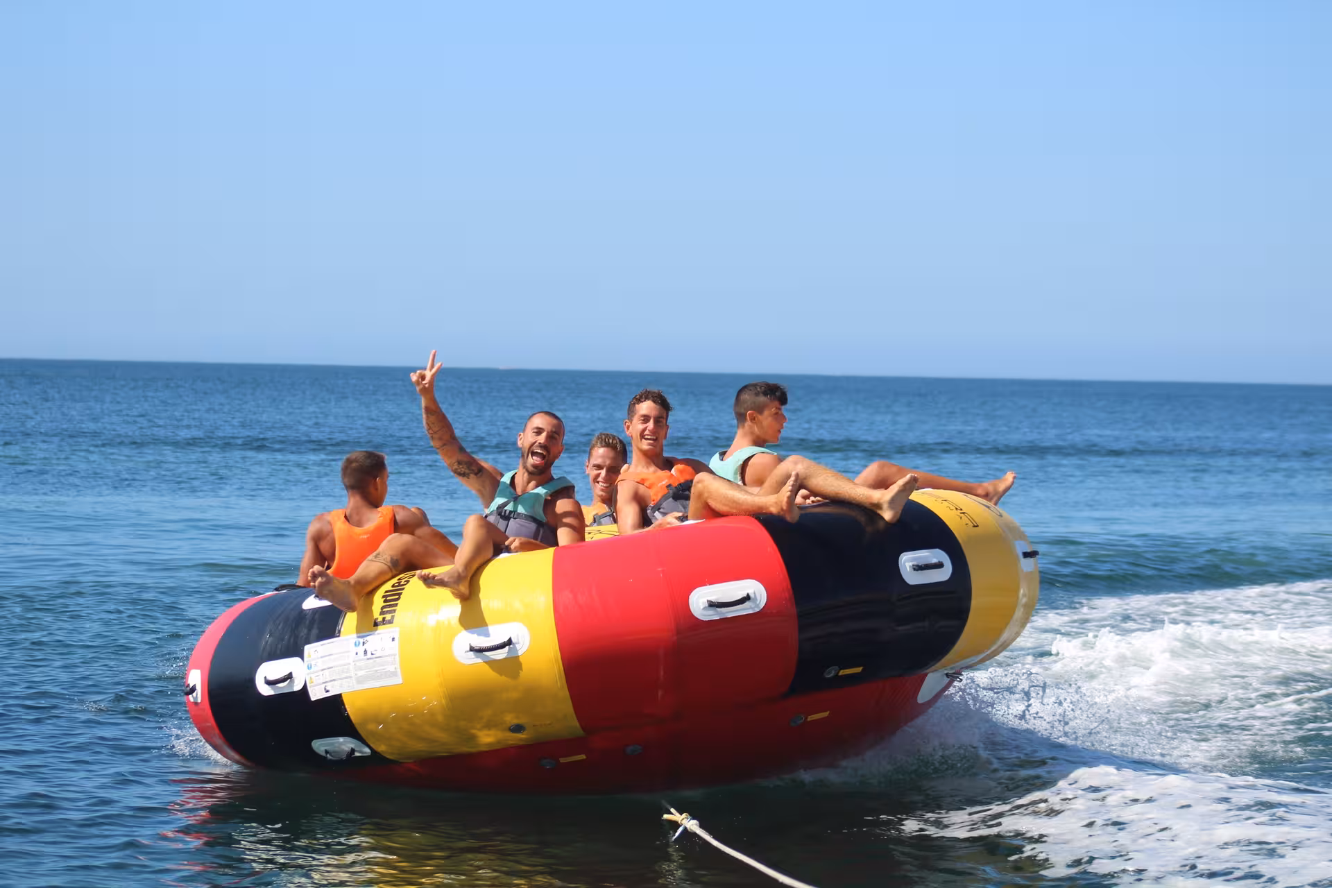 Excited group of friends riding the Twister inflatable tube on open ocean waters during a thrilling water sports adventure