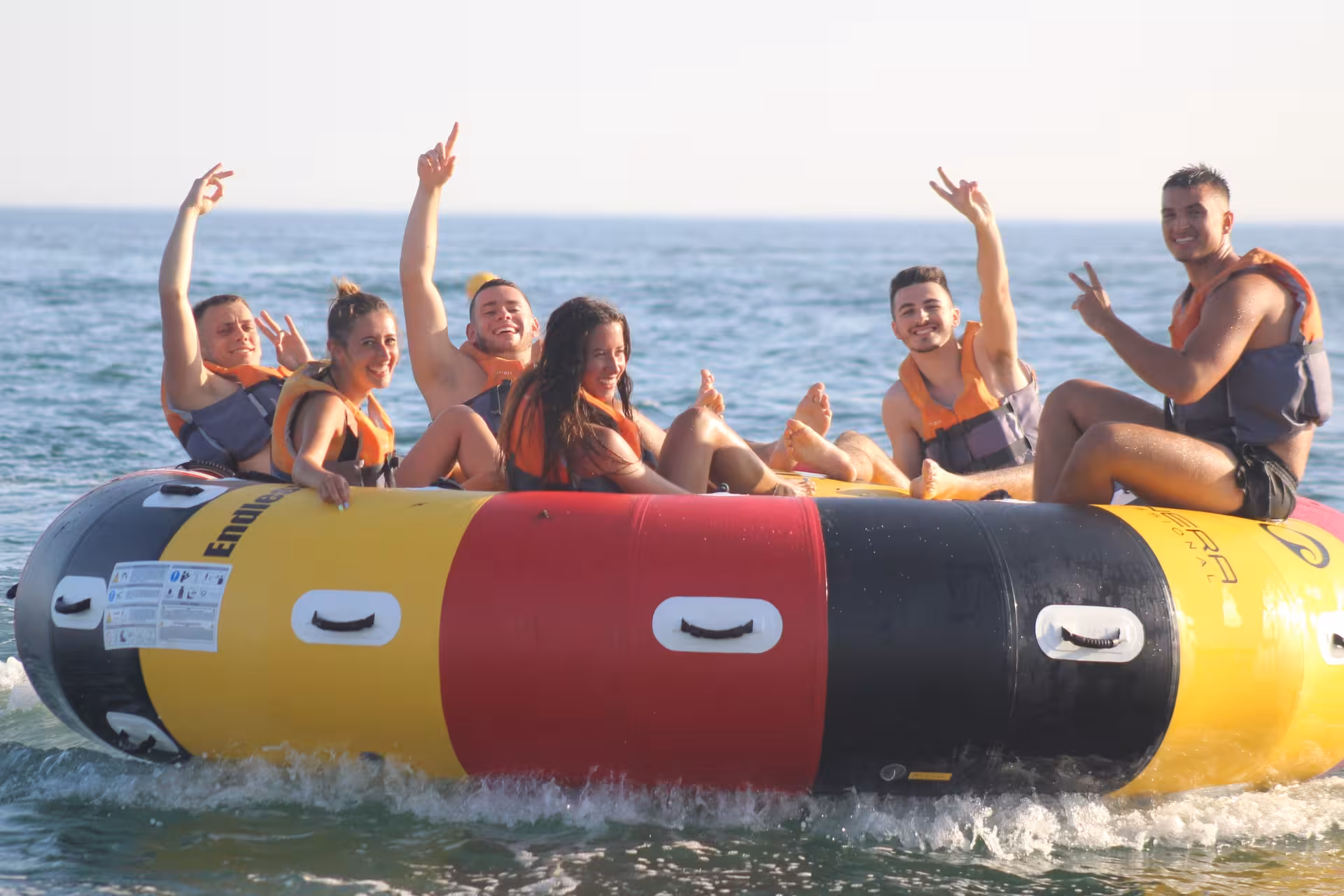 Excited group of friends wearing life jackets cheering on a colorful Twister inflatable tube ride on the ocean