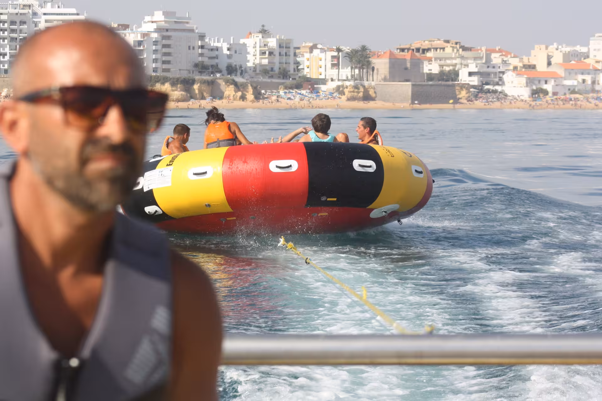 Instructor watches group being towed on inflatable Twister tube behind speedboat along Algarve coastline.