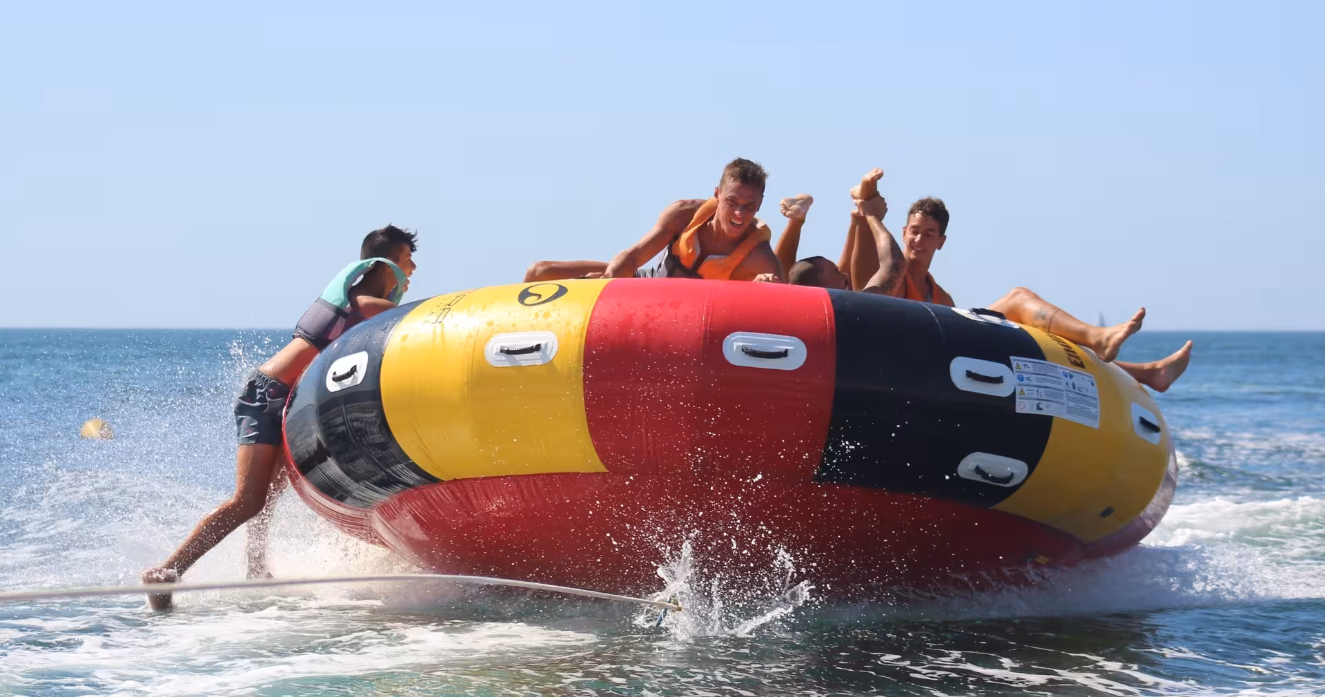 Group of riders holding on as the Twister inflatable tube spins and splashes across the sea on an action-packed water tour
