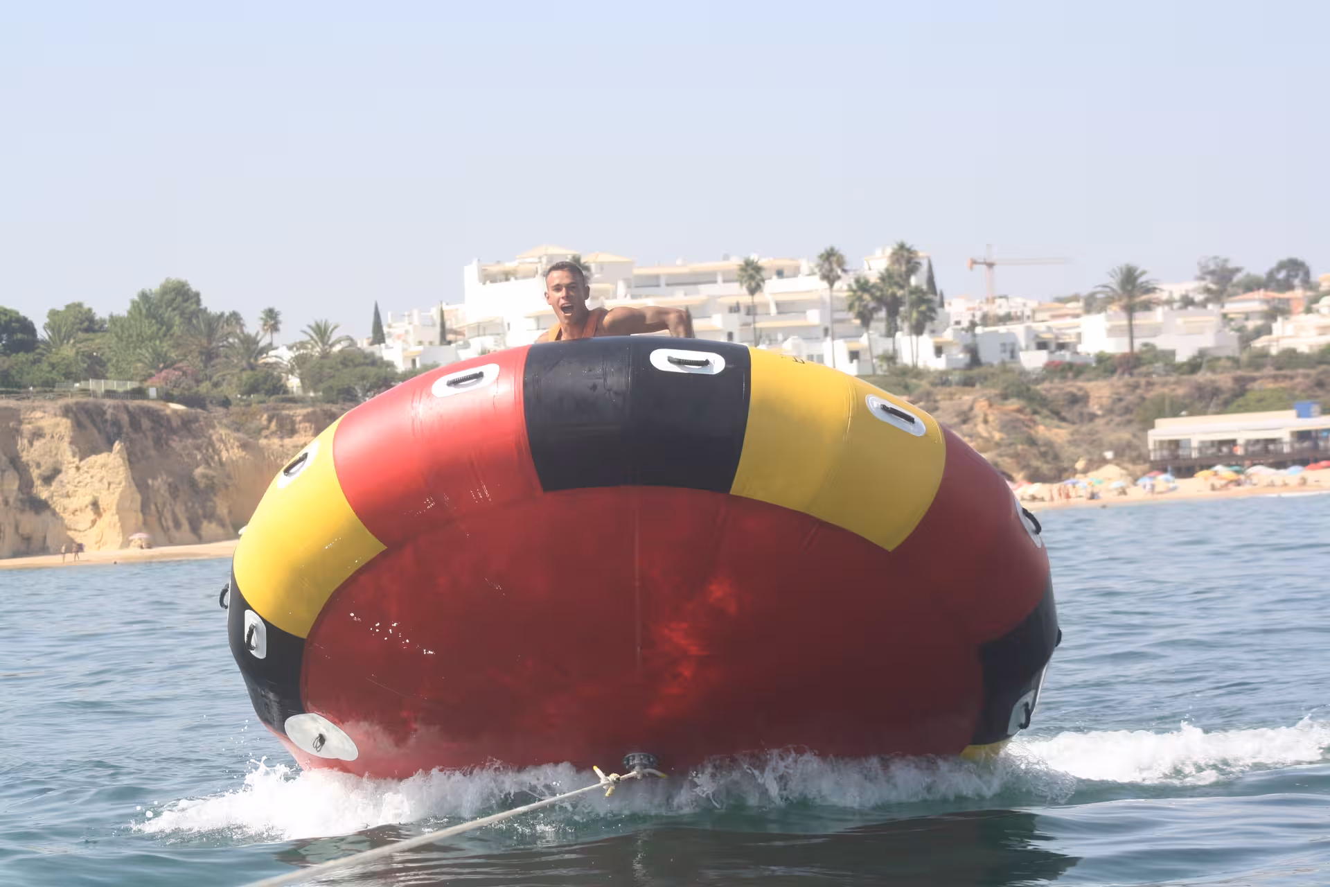 Thrilling Twister inflatable water tube ride spinning on the sea with Algarve coastal cliffs and beach in the background
