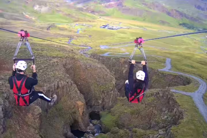 Two people zipline over a scenic canyon landscape, showcasing an adventurous ride with stunning views.