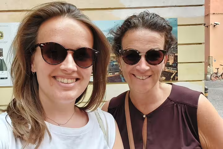 Two smiling women wearing sunglasses on a sunny street in Bologna, Italy