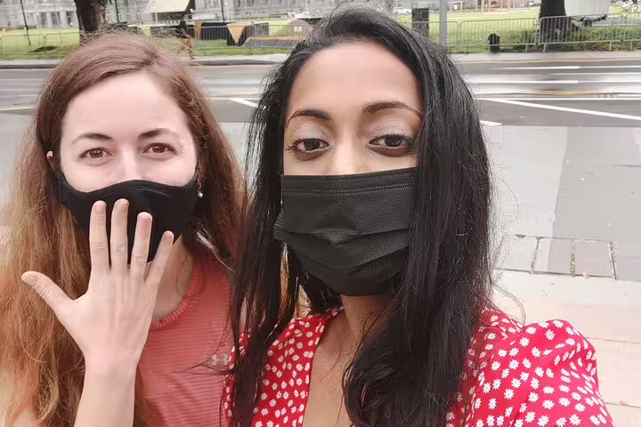 Two women wearing black face masks taking a selfie outdoors on a city street