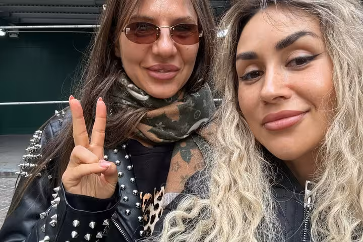 Two women taking a selfie outdoors in NYC, one flashing a peace sign wearing a studded leather jacket