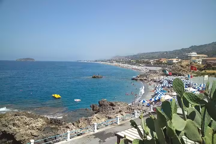 Sun-soaked Tyrrhenian Cosentino coastline with rocky cliffs, umbrellas and swimmers, seen on a private historical walking tour