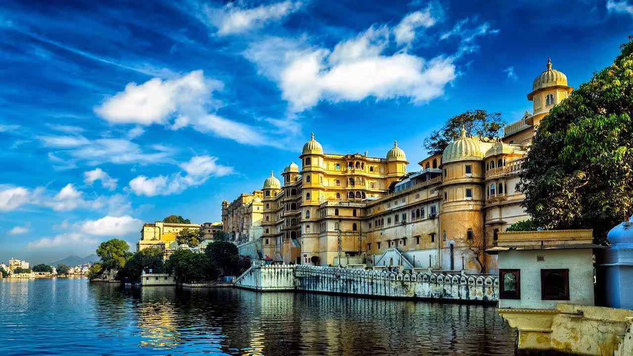 Scenic view of Udaipur's City Palace reflecting in the serene lake under a vibrant blue sky, ideal for travel enthusiasts.