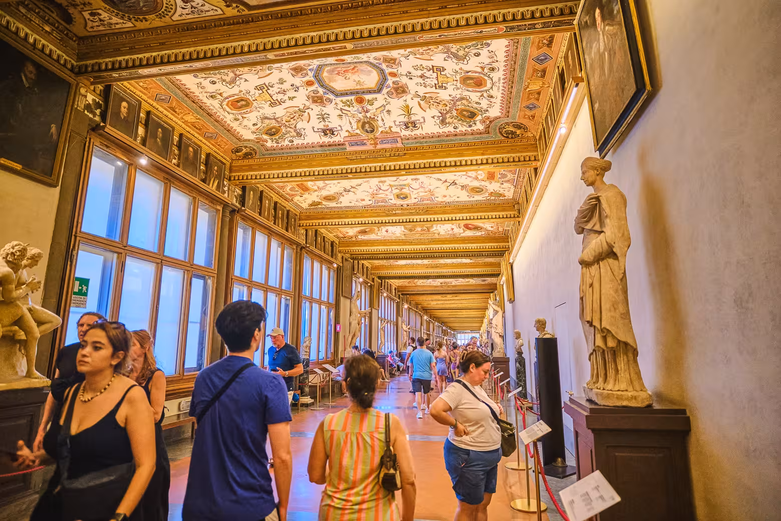 Tourists admire sculptures and art in a magnificent hallway during Uffizi Gallery private tour, enjoying skip the line benefits.