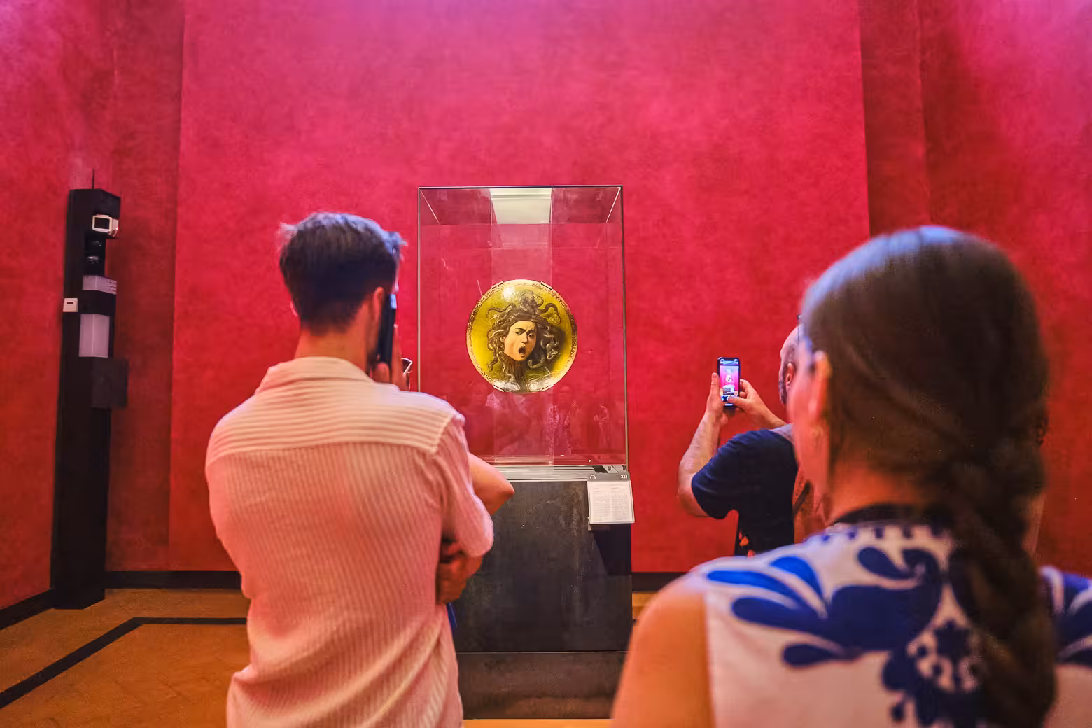 Visitors admire Medusa shield in Uffizi Gallery's vibrant red room during private tour with skip-the-line access.