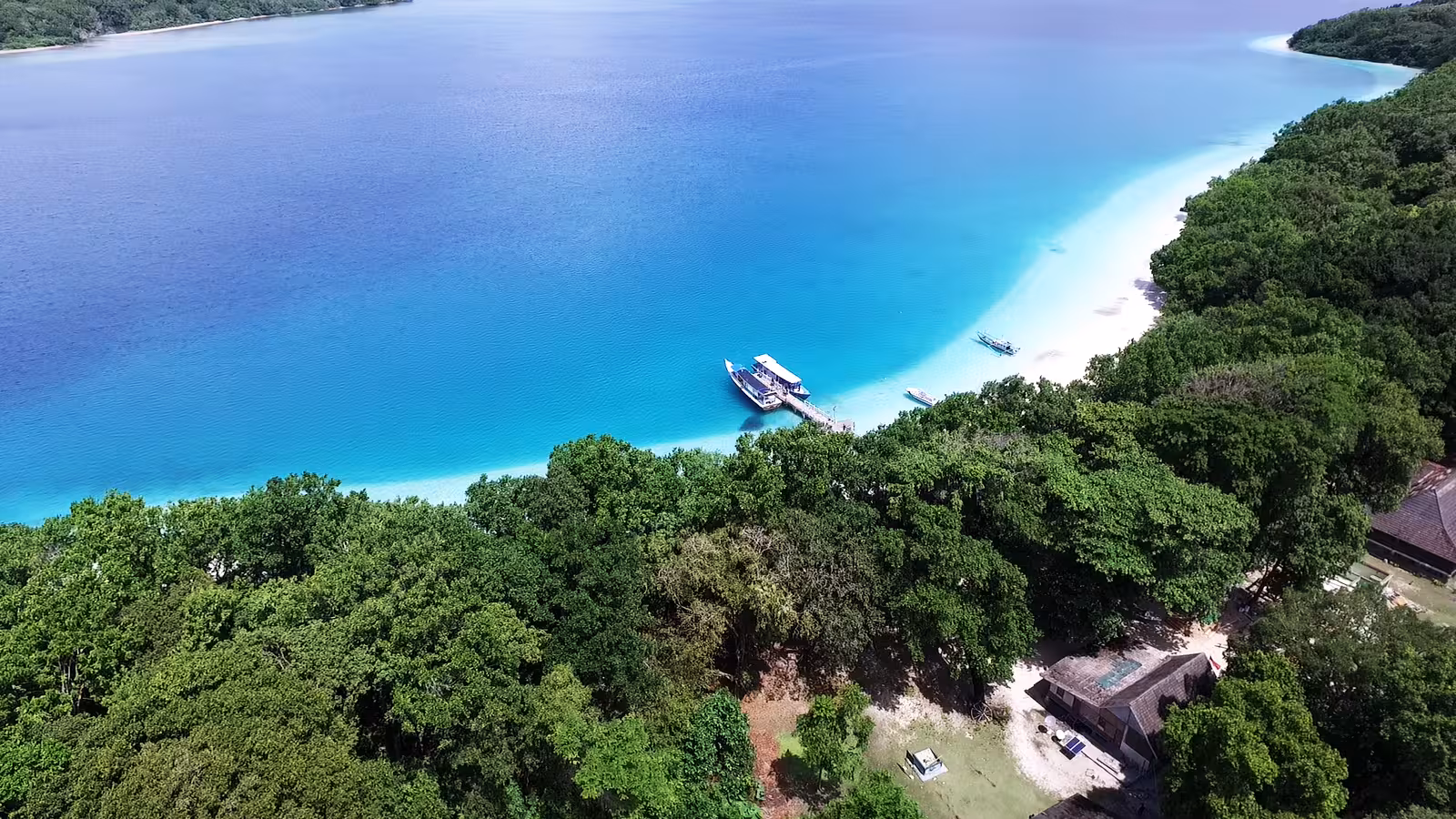 Aerial view of turquoise bay and white-sand beach with boats, Ujung Kulon National Park island excursion