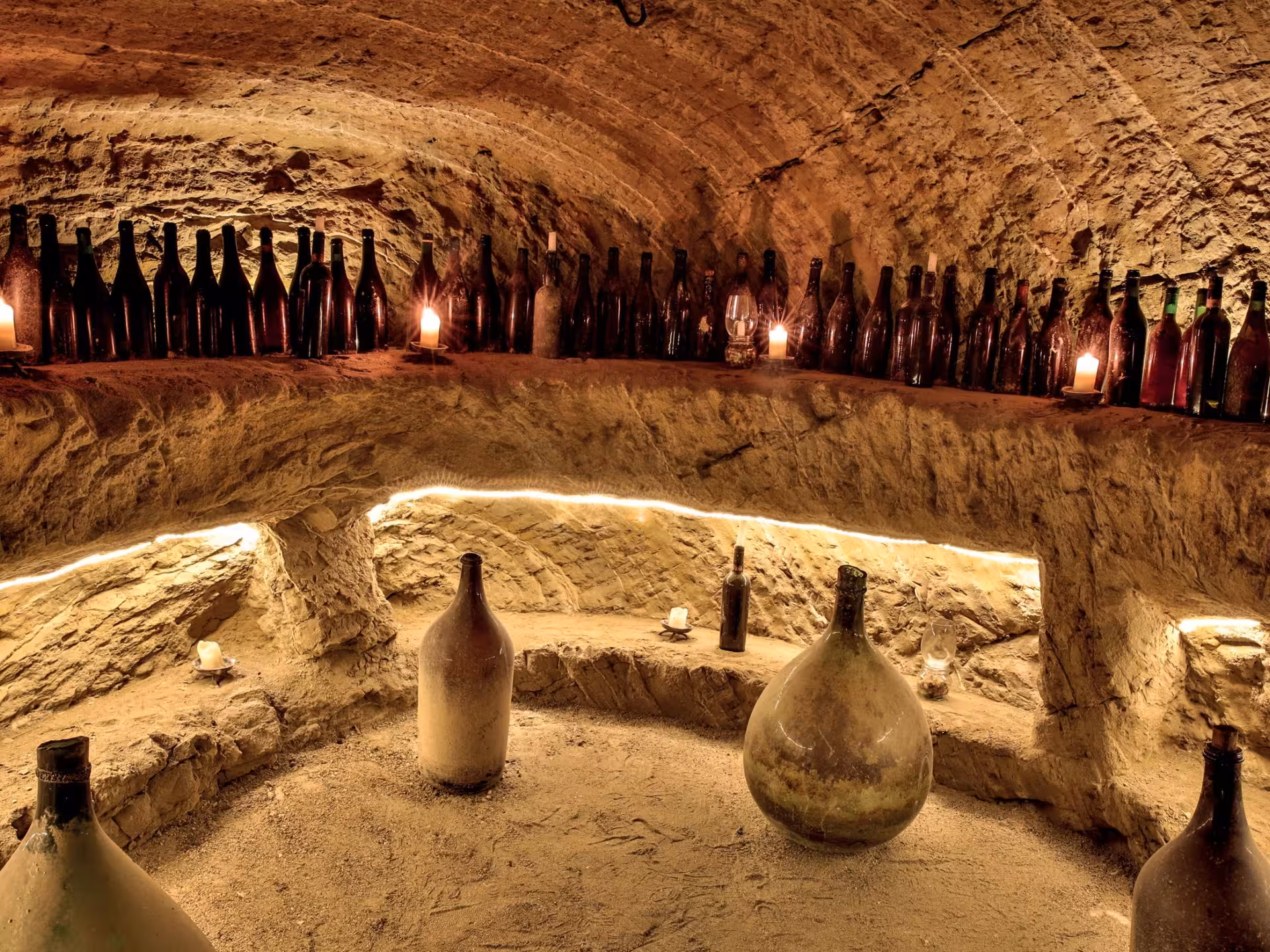 Dimly lit underground cave near Asti with vintage wine bottles and candles, creating a rustic ambiance.