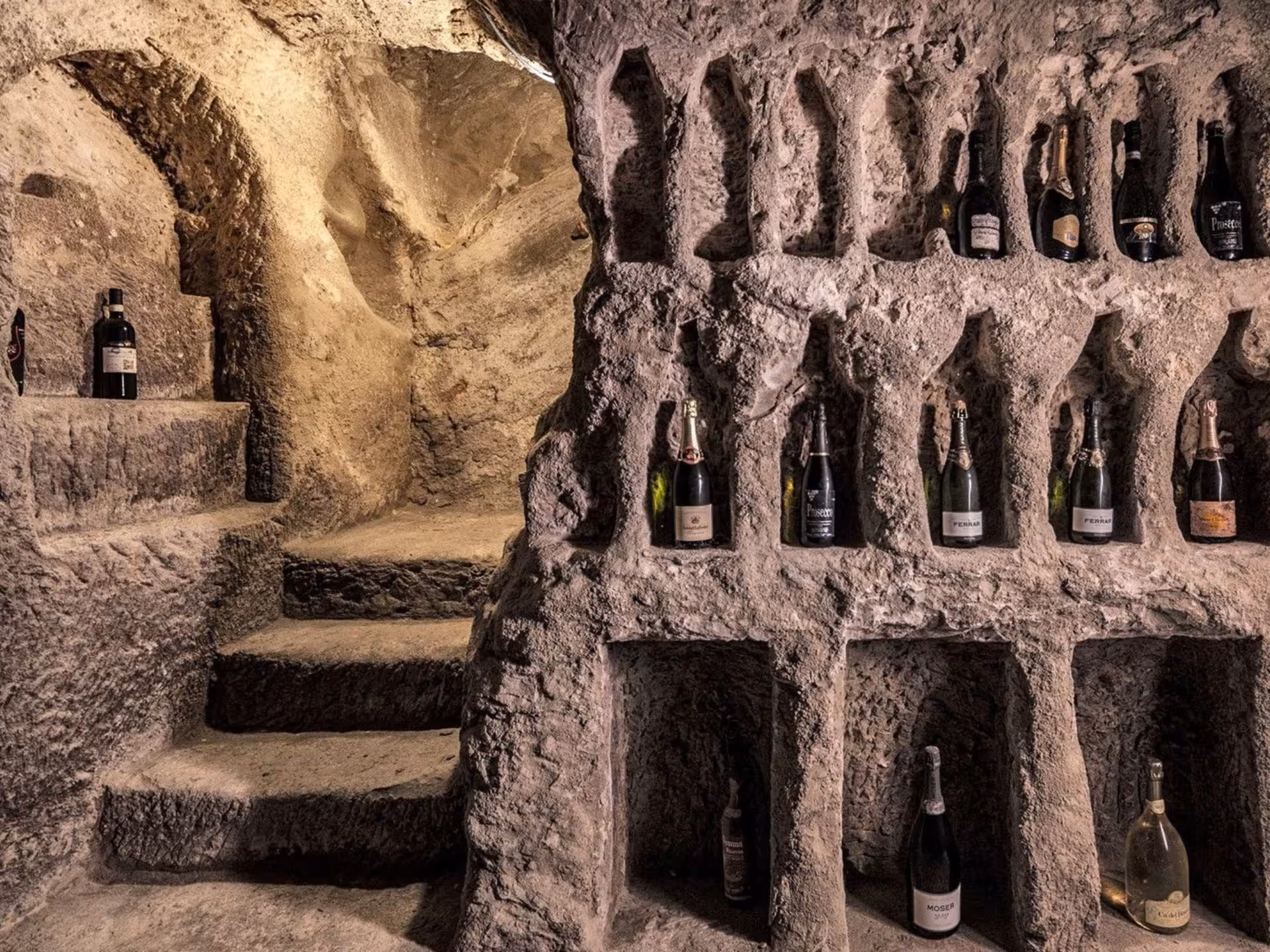 Explore a historic underground cave near Asti with wine bottles displayed in stone niches during a food and wine tasting tour.