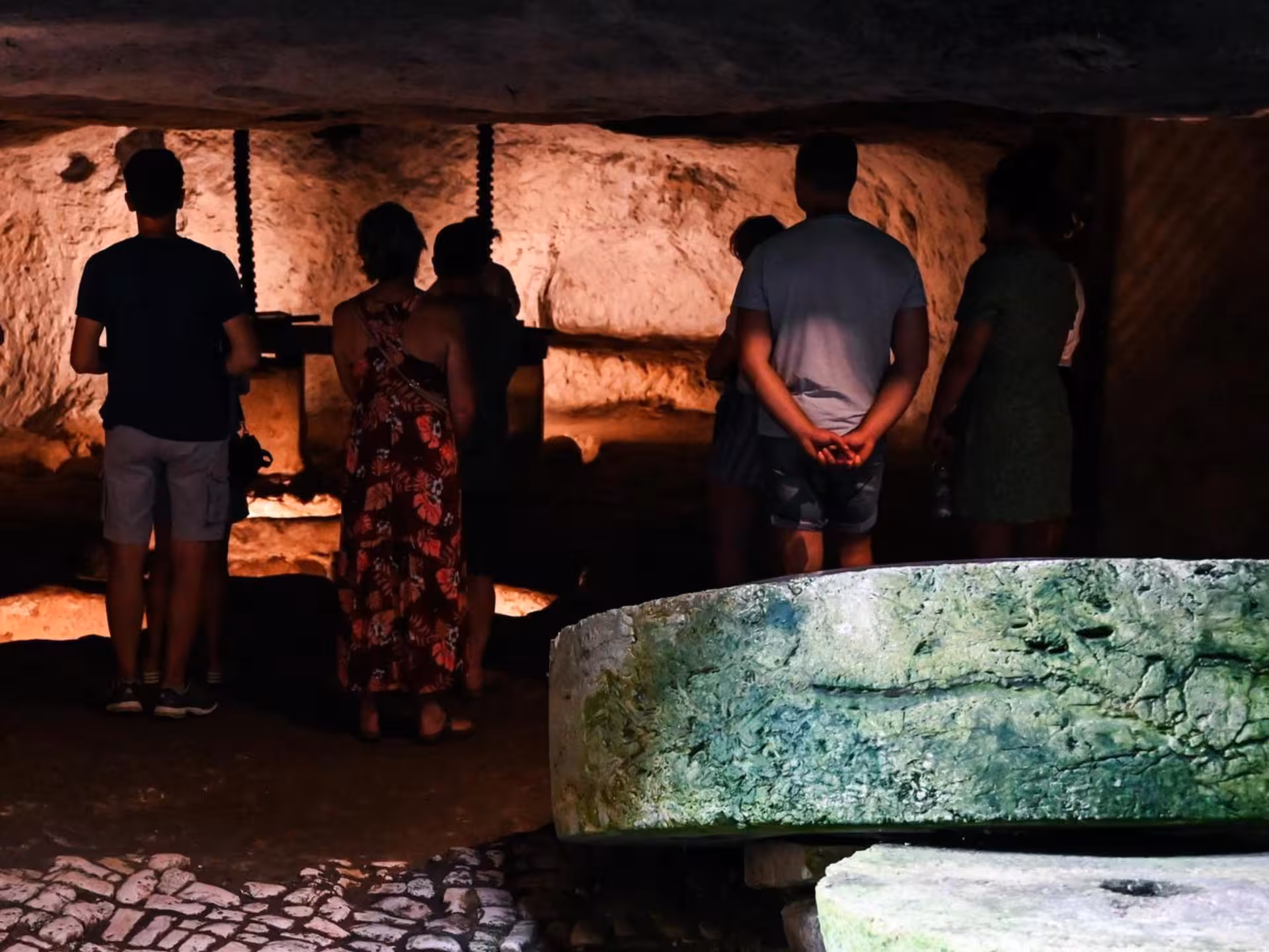 Visitors explore the historic underground olive mill near Otranto, illuminated with warm lighting.