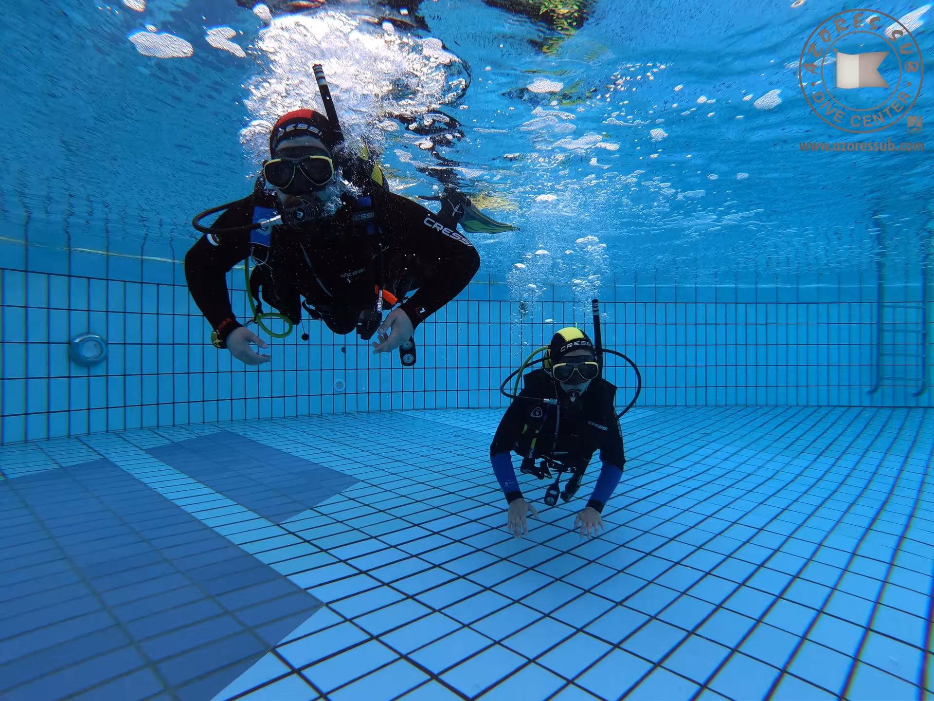 Underwater swimming pool baptism experience with scuba instructors, bubbles rising over tiled pool floor