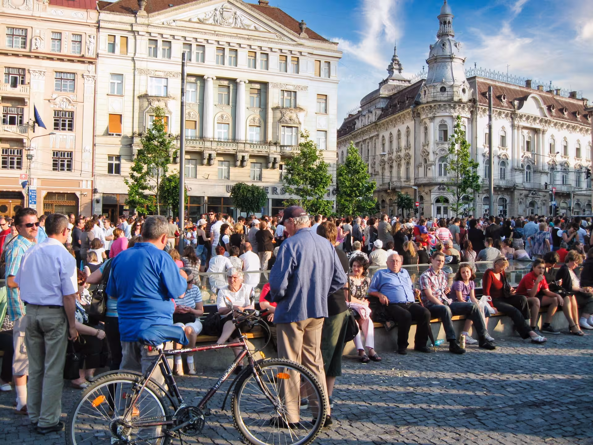 Lively crowd gathering in Cluj-Napoca's historic Unirii Square with ornate Austro-Hungarian buildings on guided walking tour