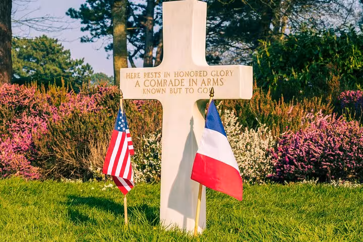 Unknown soldier grave at Normandy American Cemetery with US and French flags among colorful flowers
