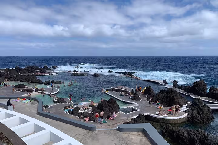 Tourists swim in natural volcanic pools by the ocean, offering breathtaking views on The Untraveled West Tour.