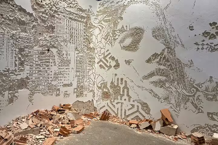 Intricate urban art mural in Lisbon showcasing a textured wall with a face and cityscape design amidst scattered bricks.