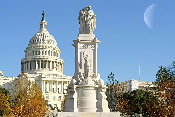 US Capitol Building dome with Peace Monument statue under blue sky in Washington DC