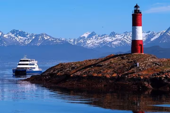 Tour boat approaches Les Eclaireurs Lighthouse with snow-capped mountains in the background, Beagle Channel, Ushuaia.