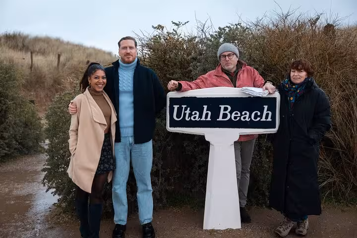 Four visitors posing beside Utah Beach sign on a D-Day Normandy tour from Cherbourg