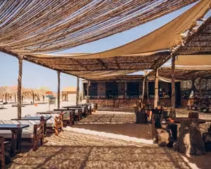Rustic open-air beach lounge with woven reed roof and wooden tables at Utopia Island, Hurghada
