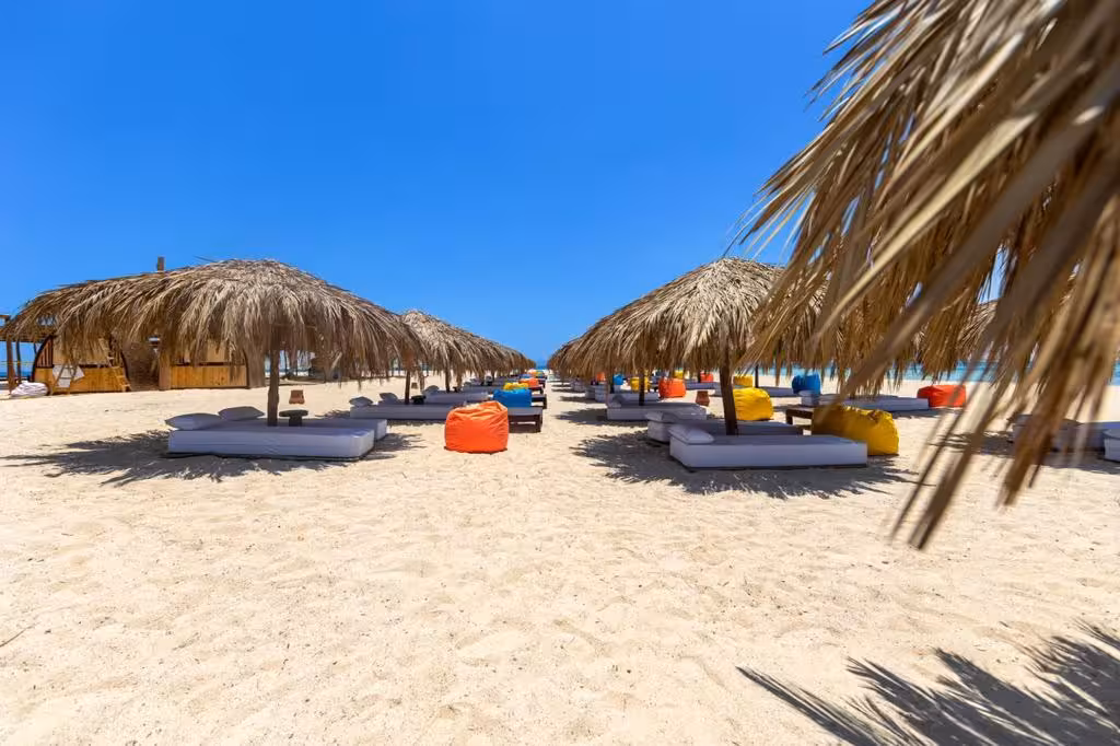 Utopia Island beach with thatched palm umbrellas, white sand, loungers, and colorful bean bags in Hurghada