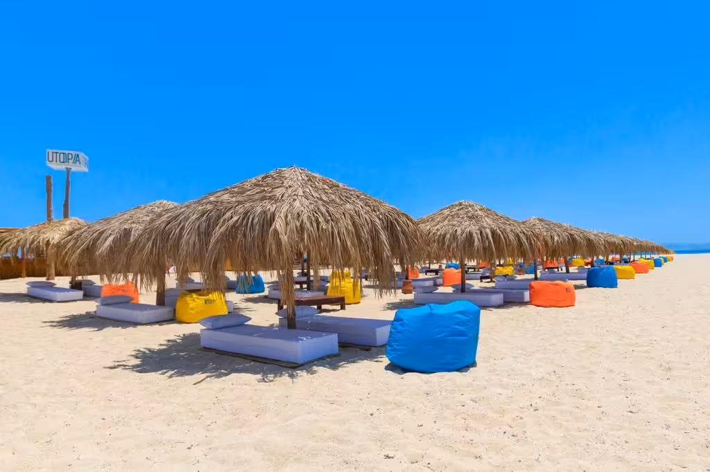 Utopia Island beach with thatched palm umbrellas, colorful bean bags, and white sand loungers in Hurghada