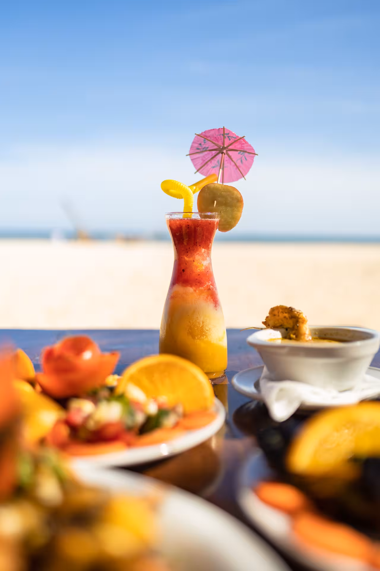 Tropical layered fruit smoothie with cocktail umbrella on beachside table with fresh fruit plates at Hurghada beach