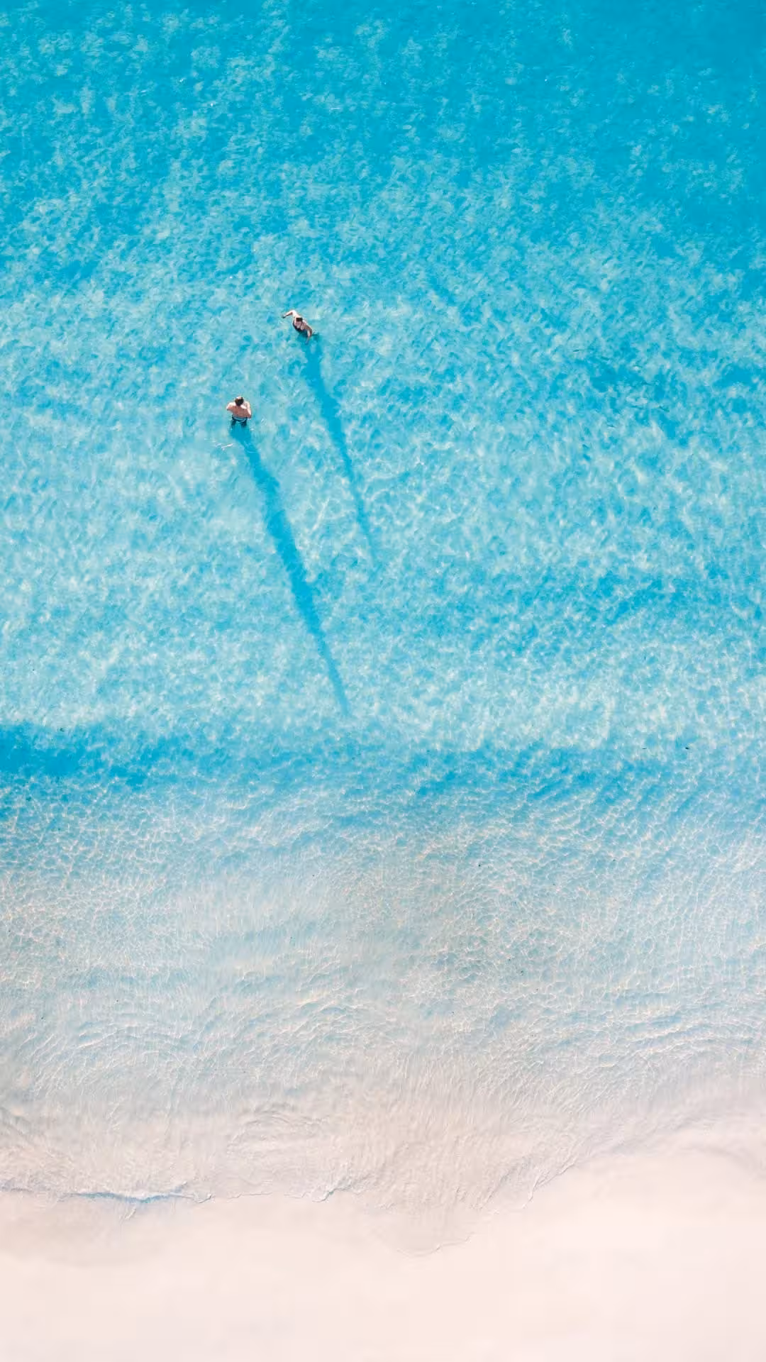 Aerial view of two swimmers in crystal clear turquoise waters near a white sandy beach in Hurghada