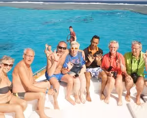 Group of tourists sitting on boat bow at Utopia Island with turquoise Red Sea waters and snorkeling area behind
