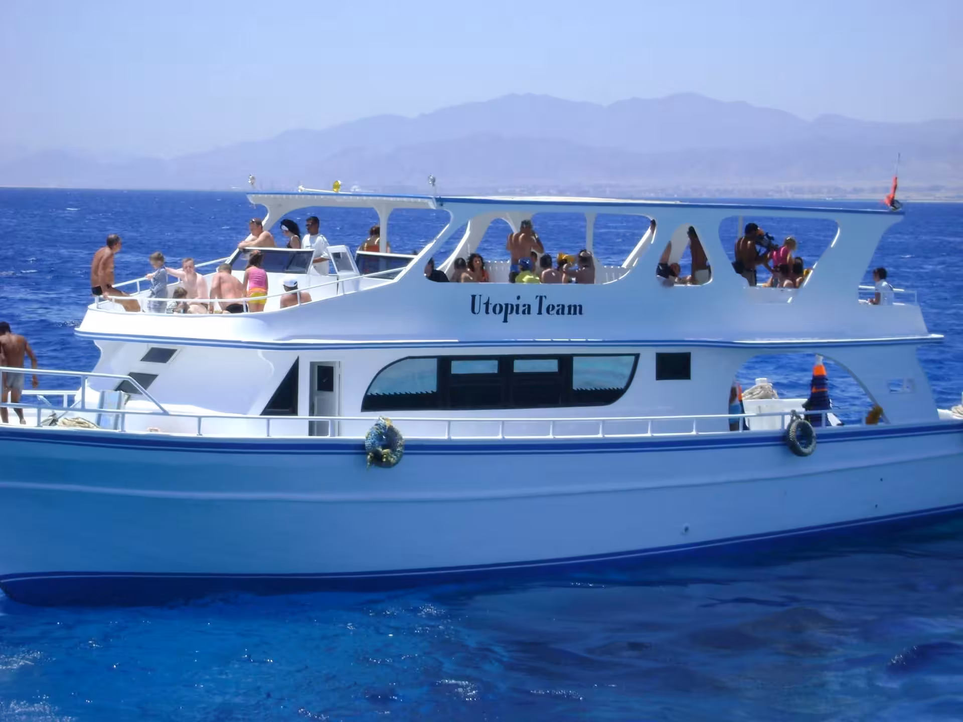 Utopia Team boat filled with tourists on blue Red Sea waters near Hurghada with mountains in background