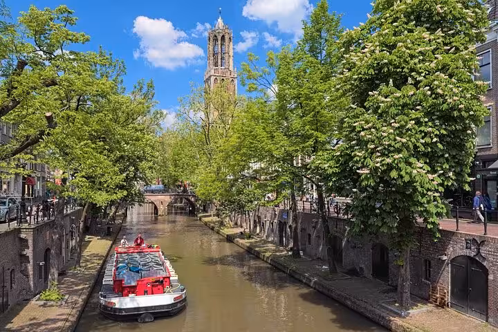 Canal boat on Utrecht's Oudegracht with Dom Tower rising above tree-lined medieval wharf cellars