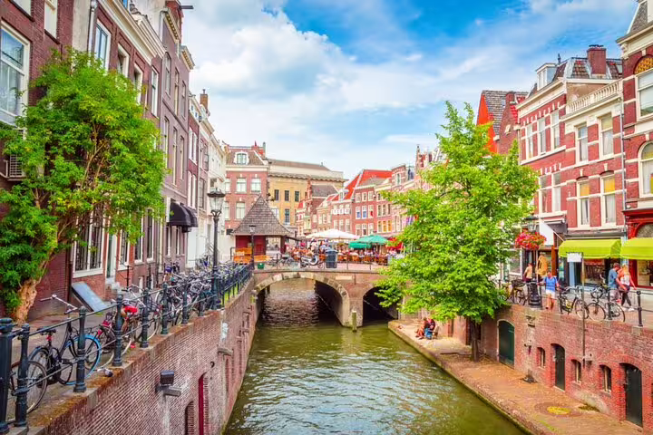 Historic Utrecht canal with brick buildings, arched bridge, and bicycles on a sunny day