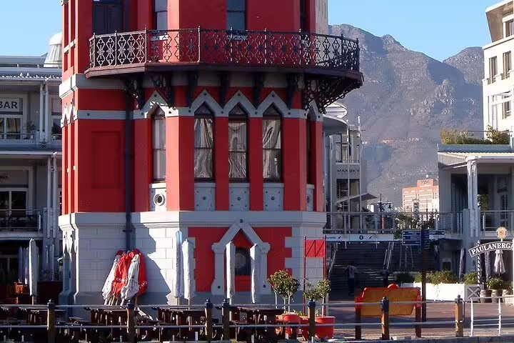 Vibrant red and white building at V&A Waterfront, Cape Town, with mountains in the background, near Robben Island tours.