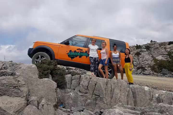 Group of women posing by an orange SUV on a rocky terrain near Vai Beach on a VIP adventure tour.