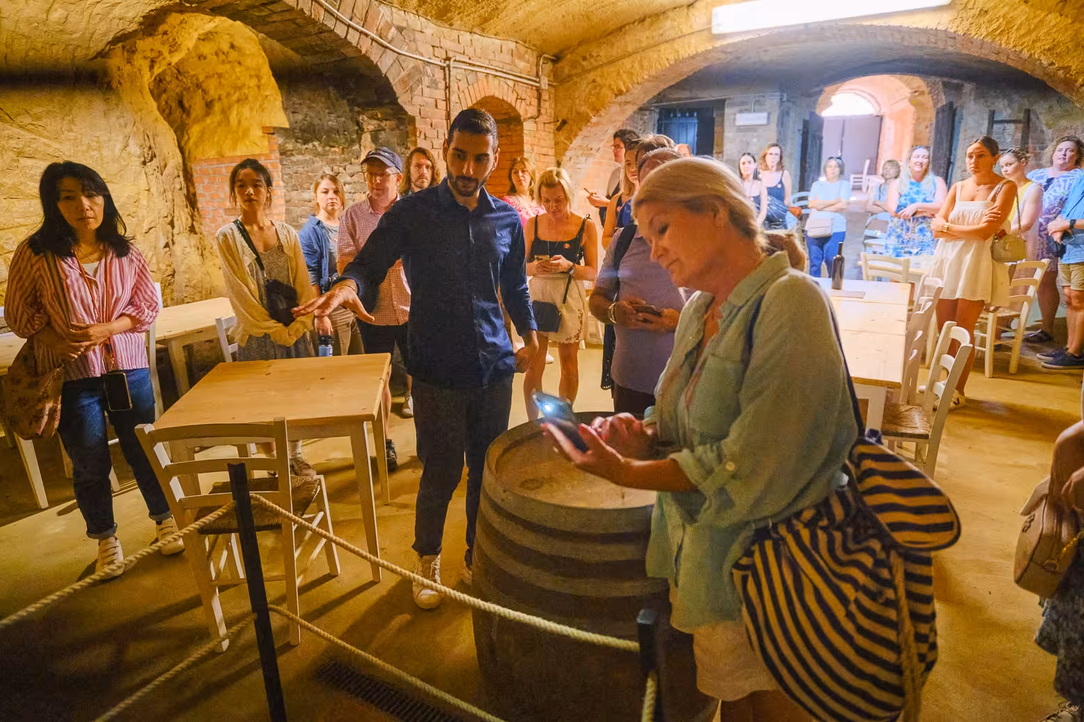 Visitors explore an ancient wine cellar in Val D'Orcia during a guided tour with wine and cheese tasting experience.