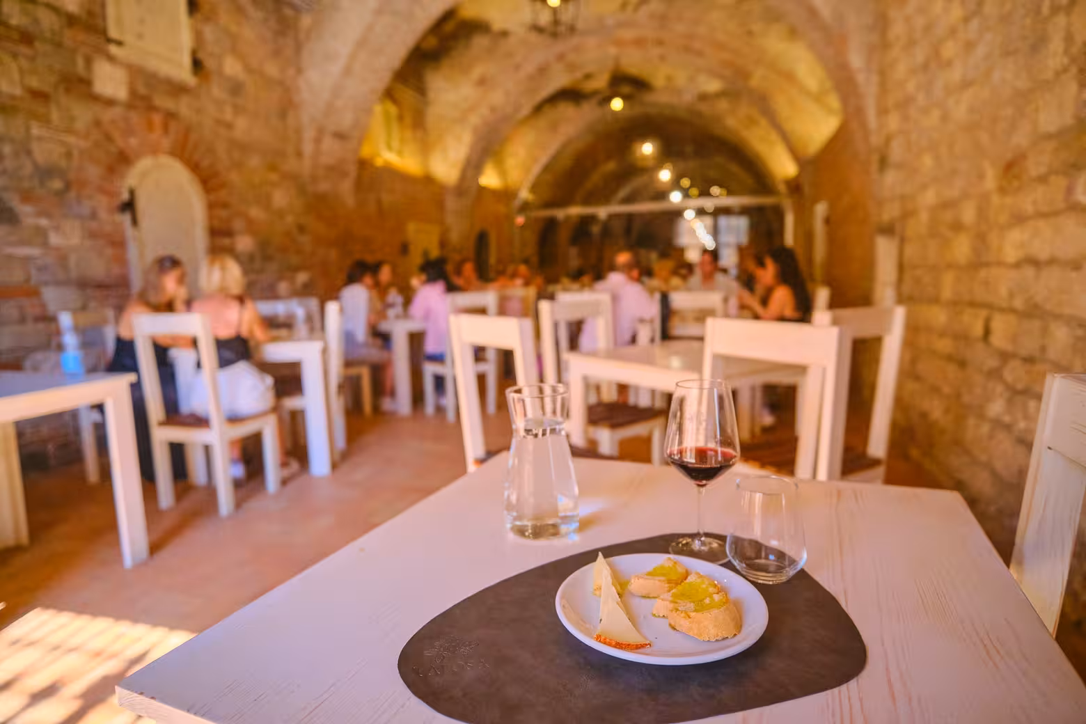 A plate of cheese and bread with wine set on a table in a charming, rustic tasting room in Val D'Orcia.