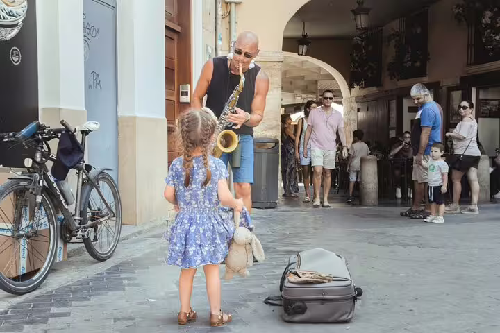 A street musician plays saxophone for a young girl in a charming Valencian alley, perfect for a fun family tour adventure.