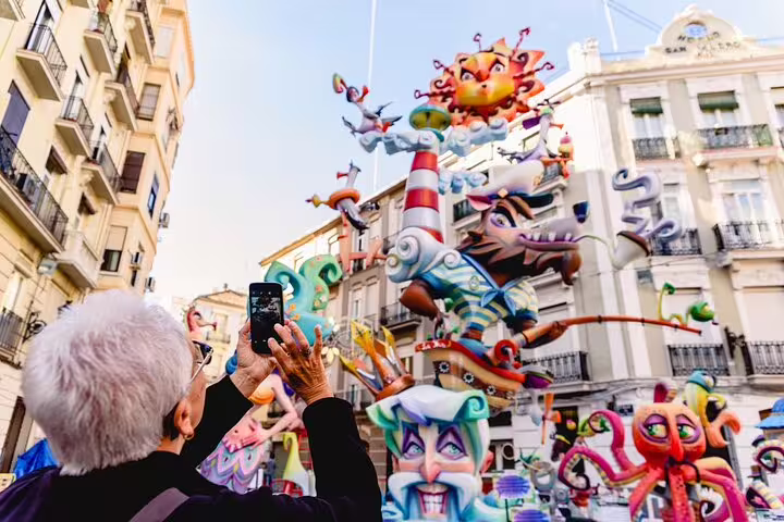 Elderly tourist captures vibrant Fallas sculptures during Valencia Private Family Tour, showcasing local cultural festivities.