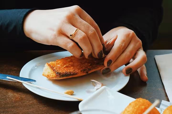 Close-up of hands breaking toasted bread with olive oil, a classic Valencia tapas tasting on the food tour