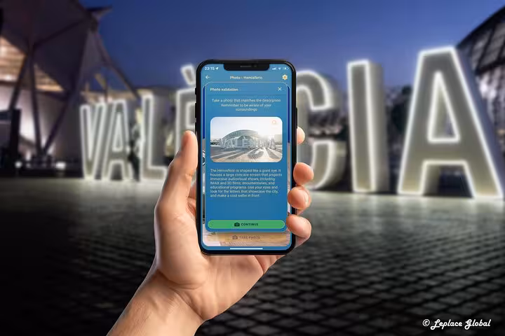 Hand holding smartphone app showing photo validation feature during self-guided walking tour in Valencia Spain