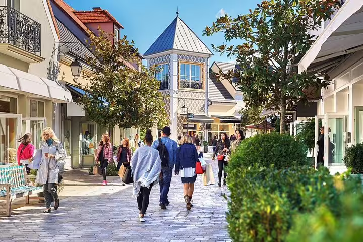 Shoppers strolling along the open-air pedestrian promenade at Vallée Village outlet shopping center near Paris